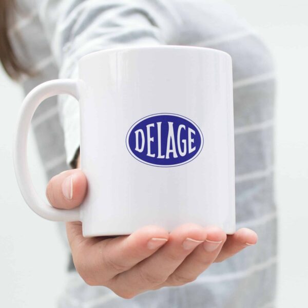 Classic white 11oz ceramic mug with Delage logo in bold blue, placed on a modern kitchen countertop.