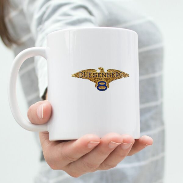White 11oz ceramic coffee mug with Duesenberg vintage car logo in gold and blue, kitchen background.
