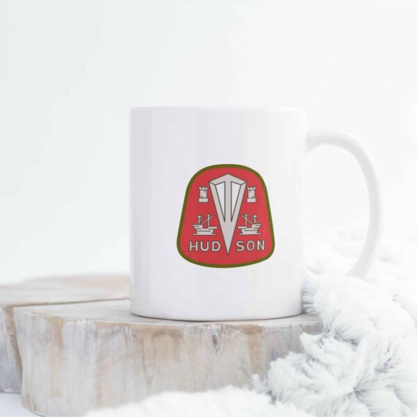 Classic white 11oz ceramic mug emblazoned with the red and green Hudson Motor Car logo, displayed on a kitchen countertop.