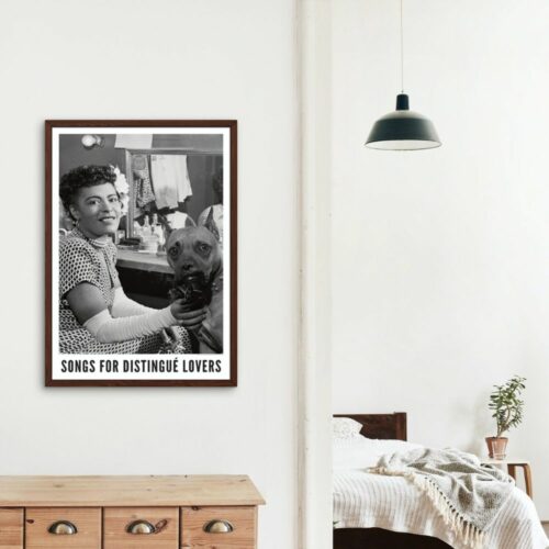 A framed poster on a wall shows a smiling Billie Holiday with a flower in her hair holding a dog, titled Songs for Distingue Lovers. Objects on a shelf include a camera, plant, books, laptop, and glass vase.