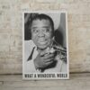 Black and white photo of Louis Armstrong with an exuberant expression playing a trumpet, phrase WHAT A WONDERFUL WORLD below, white shirt, capturing joy and music's power.