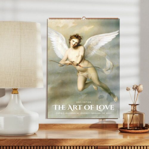 Classic style wall calendar titled The Art of Love, 2025 Edition, depicting Cupid with wings, posed with a bow and arrow, against a clouded backdrop, placed on a wooden desk beside a lamp and dried flowers.