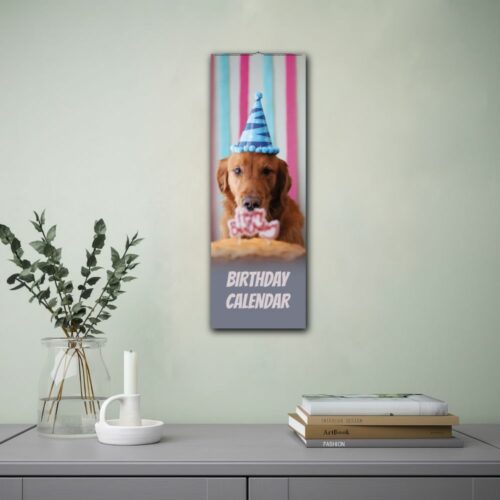 Wall calendar featuring a golden retriever wearing a blue party hat with a birthday cake in front of it. The calendar is labeled Birthday Calendar and is displayed on a wall beside a lamp and an open book, creating a cozy setting.