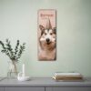 Wall calendar featuring a husky dog wearing a party hat and holding a bone-shaped chew toy in its mouth. The calendar is labeled Birthday Calendar and is displayed on a wall beside a lamp and an open book.