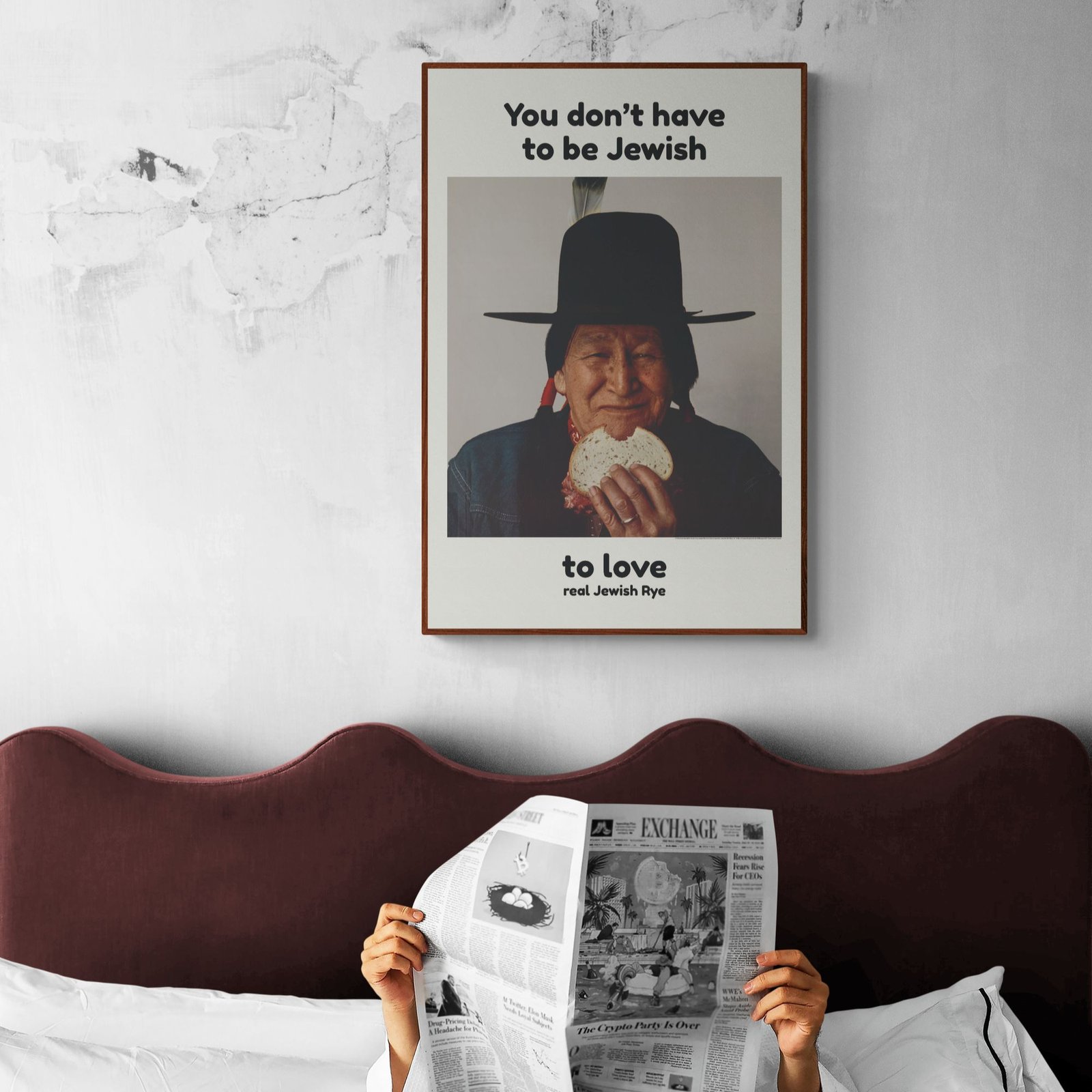 Person reading newspaper under Jewish rye bread poster.