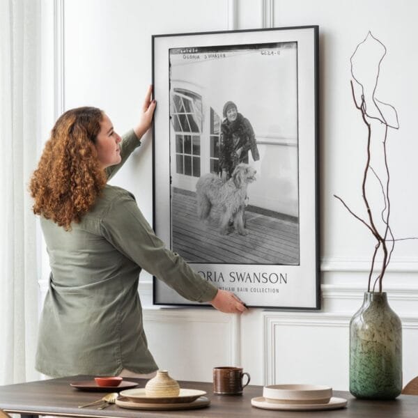 Vintage black-and-white Gloria Swanson poster featuring the Hollywood silent film star with a fluffy dog on a ship deck. Classic cinema-inspired wall art, available as a premium museum-quality print or foam board for retro decor lovers and old Hollywood enthusiasts.