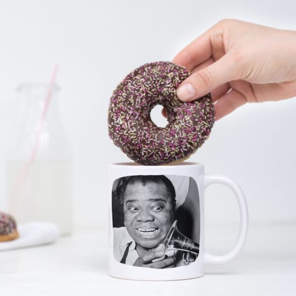 Hand holding donut over mug with Louis Armstrong photo.