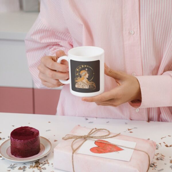 Person holding mug beside cake and gift.