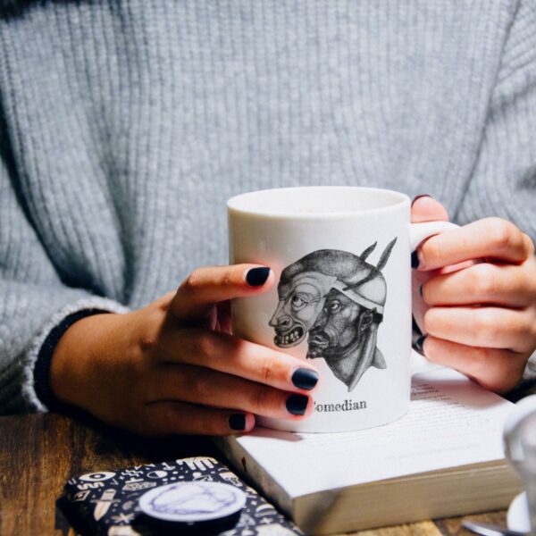 Person holds mug with masks illustration.