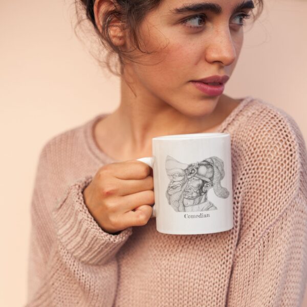 Woman holding illustrated mug, wearing pink sweater.