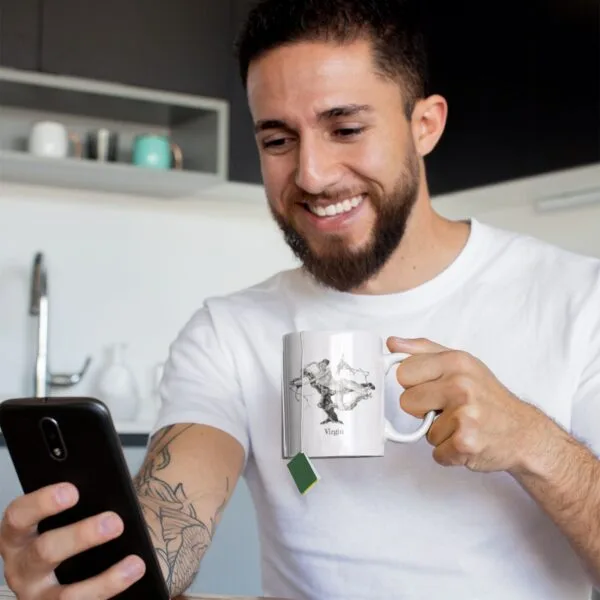 Man drinking tea and smiling at phone in kitchen.