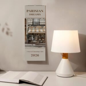 Parisian cafe-themed 2026 wall calendar beside lamp and book.