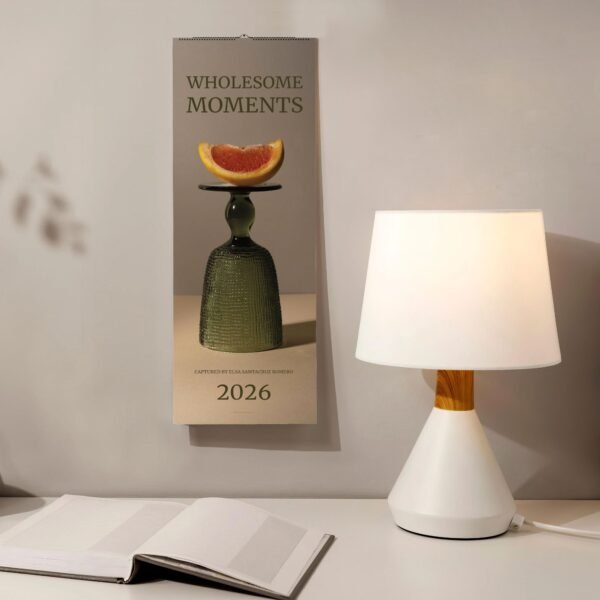 Calendar on wall beside lamp and open book.
