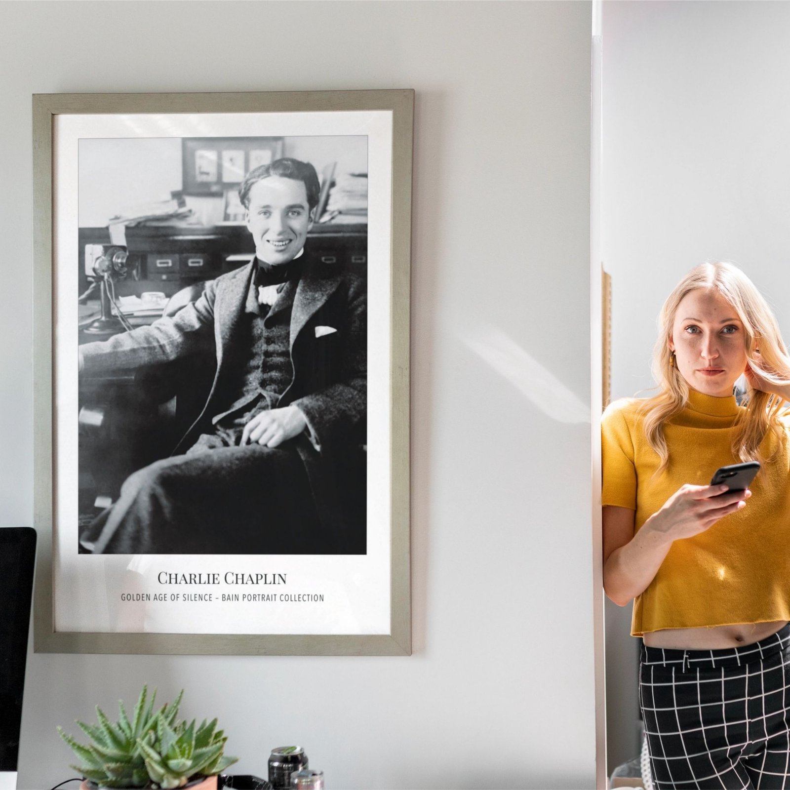 Woman with smartphone near framed Charlie Chaplin poster.