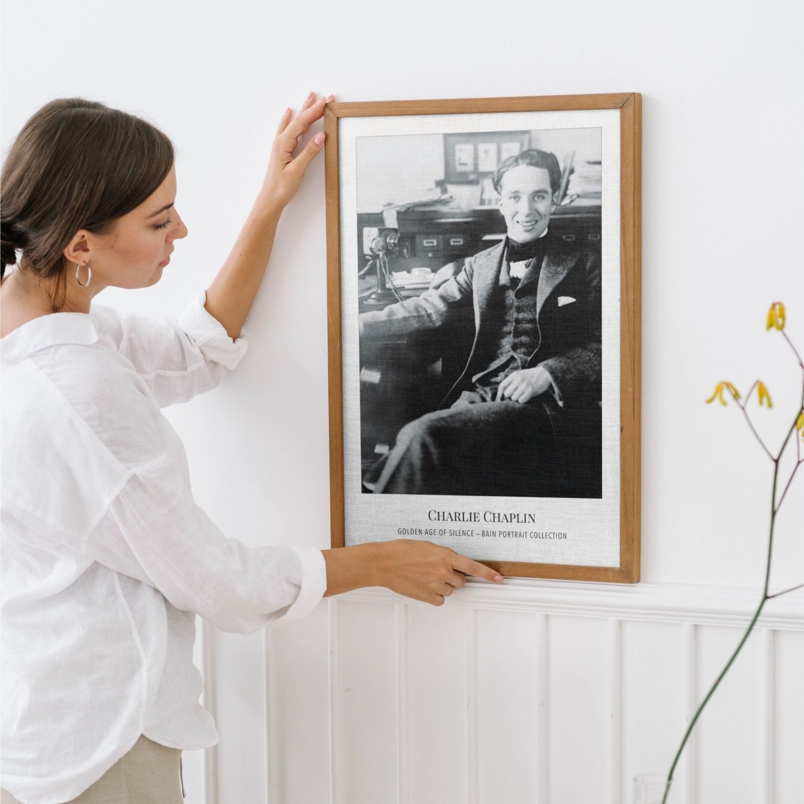 Woman adjusting framed Charlie Chaplin poster on wall.