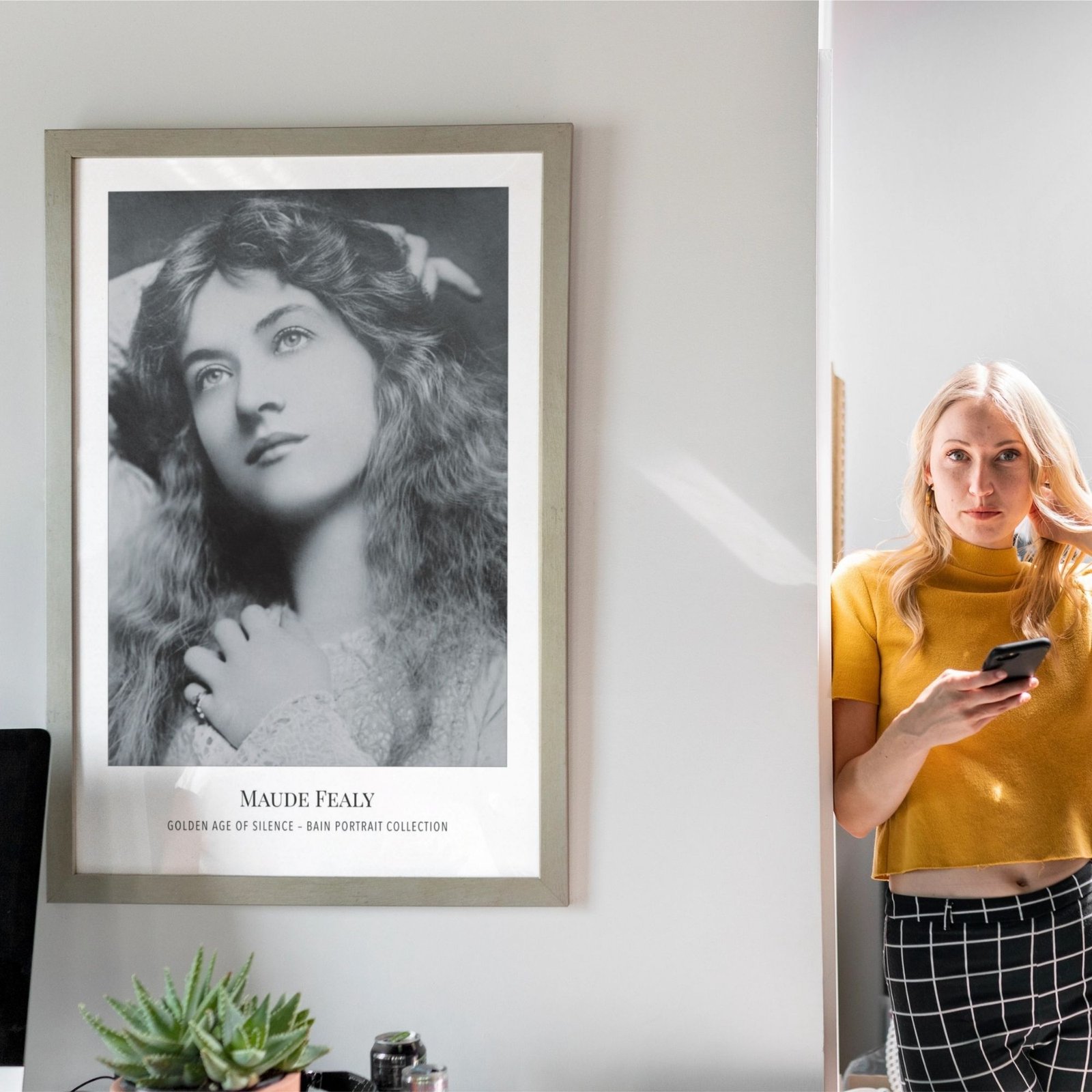 Woman stands by vintage portrait, holding smartphone.