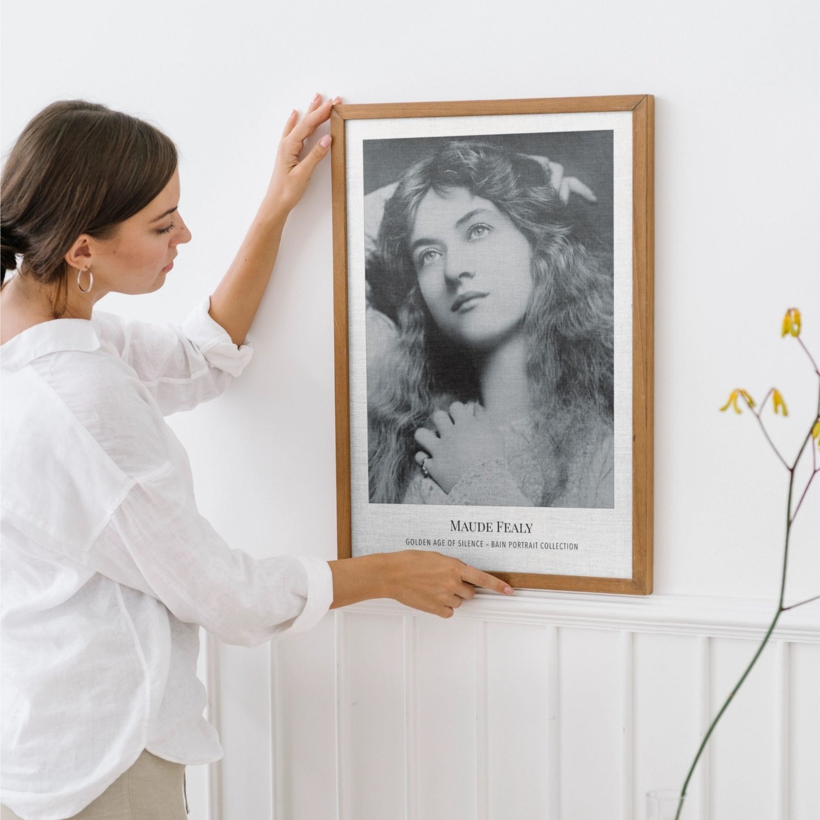 Woman hangs framed vintage portrait on wall.