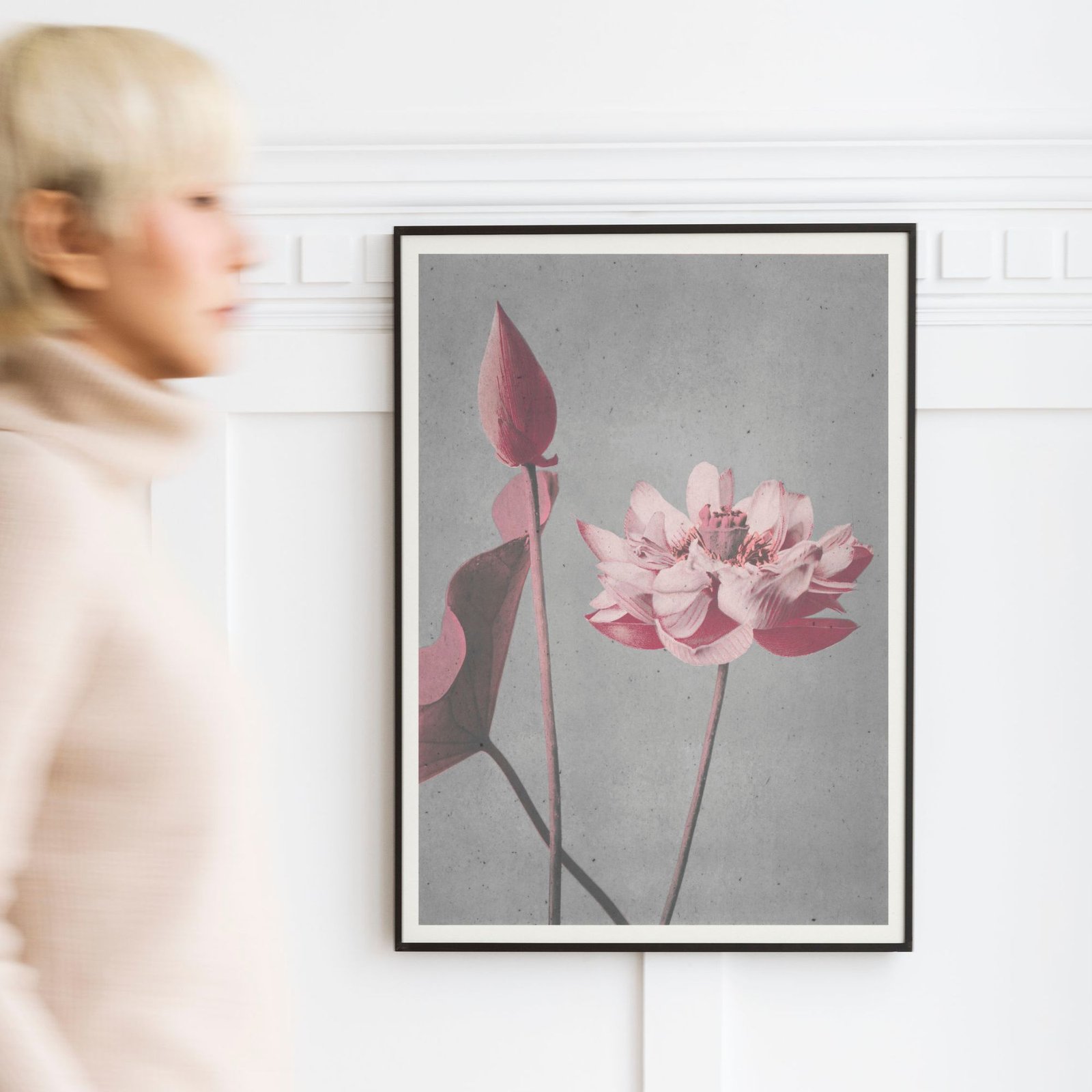 Framed floral artwork on wall with woman passing by.