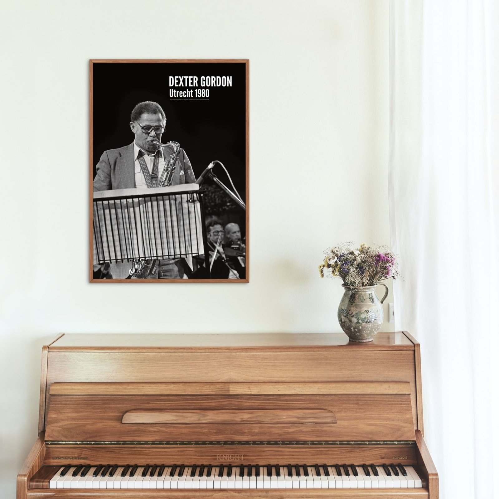Framed saxophonist photo above a wooden piano.