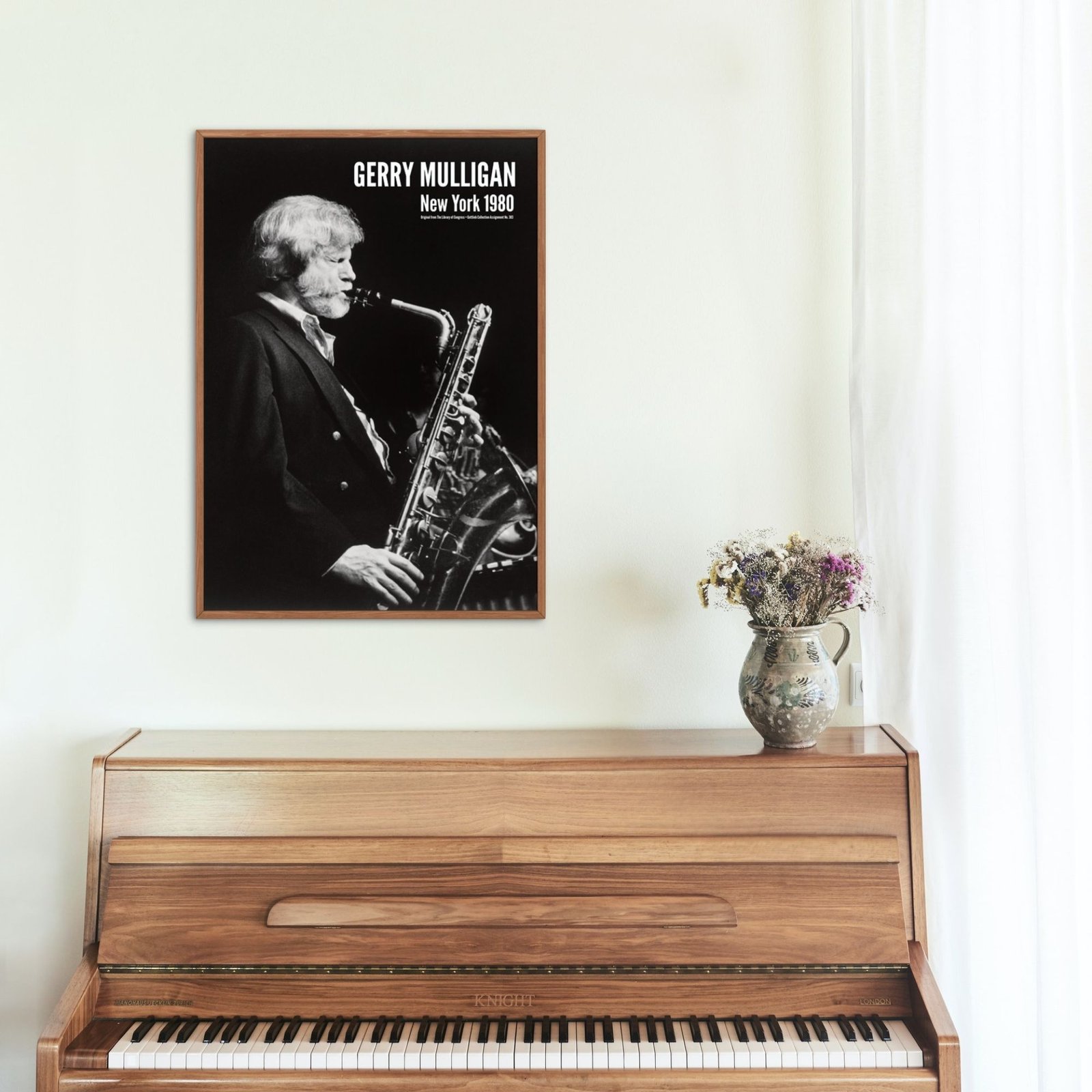 Framed saxophonist photo above wooden piano with flowers.