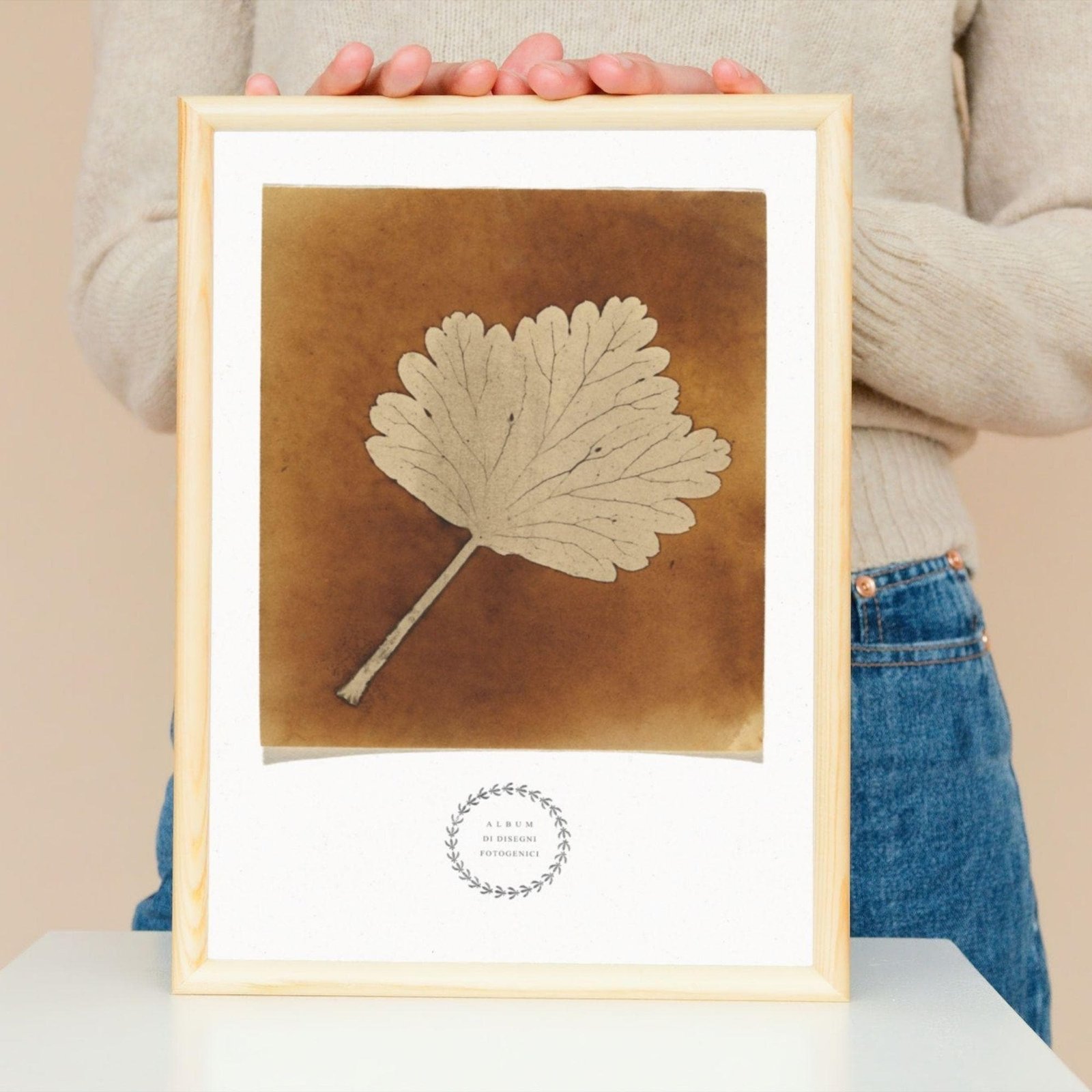Person holding framed botanical leaf illustration.