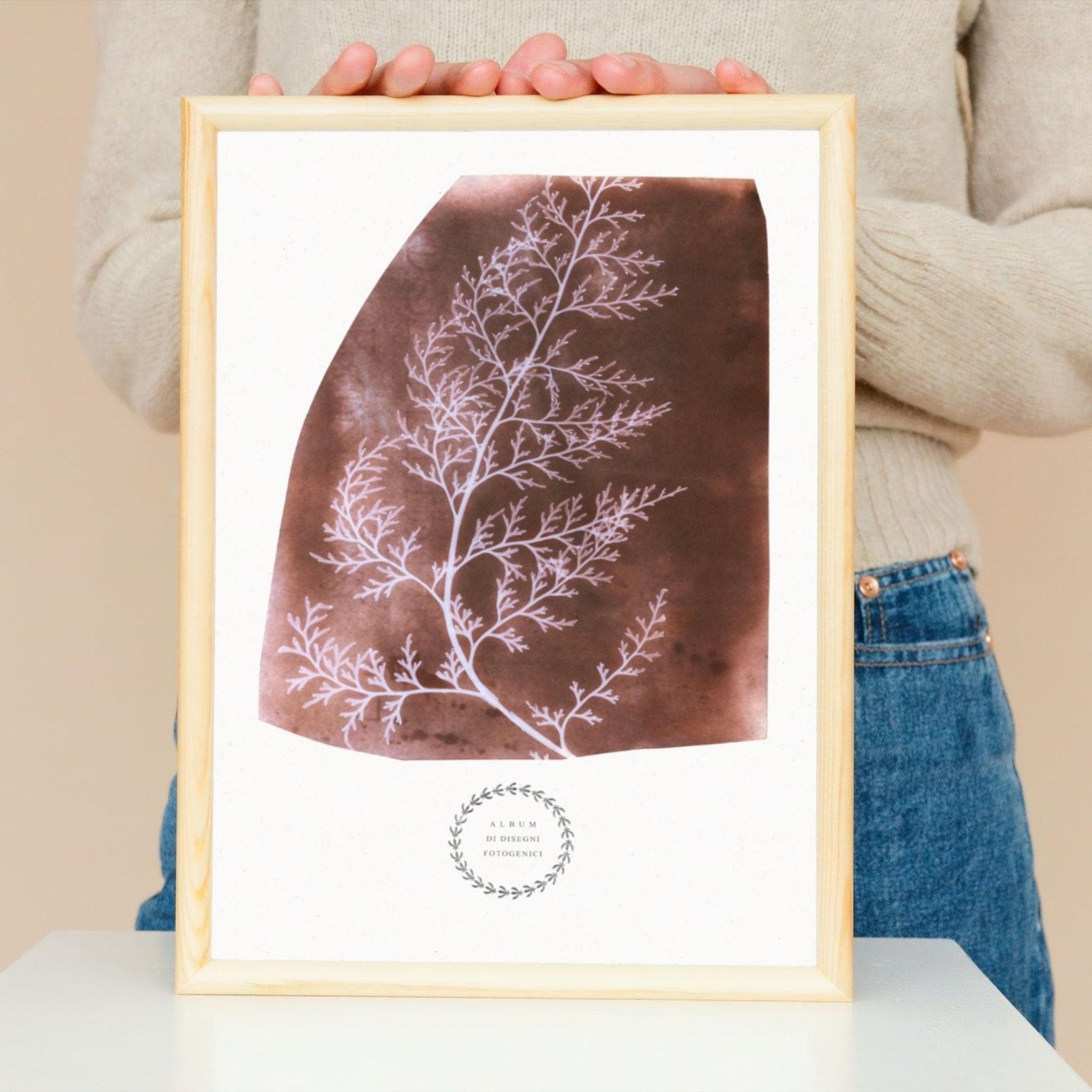 Framed botanical artwork held by person in jeans.
