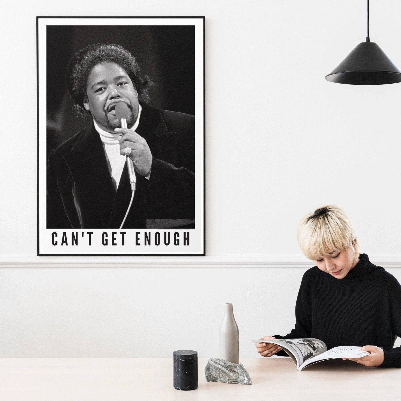 Woman reading near a singer's poster on wall.