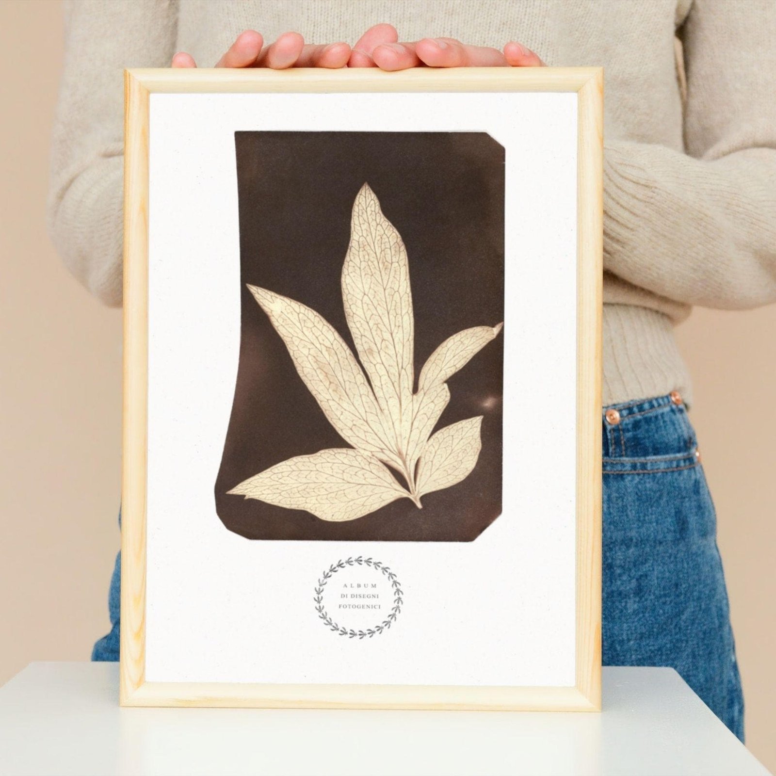 Person holding framed botanical leaf art.