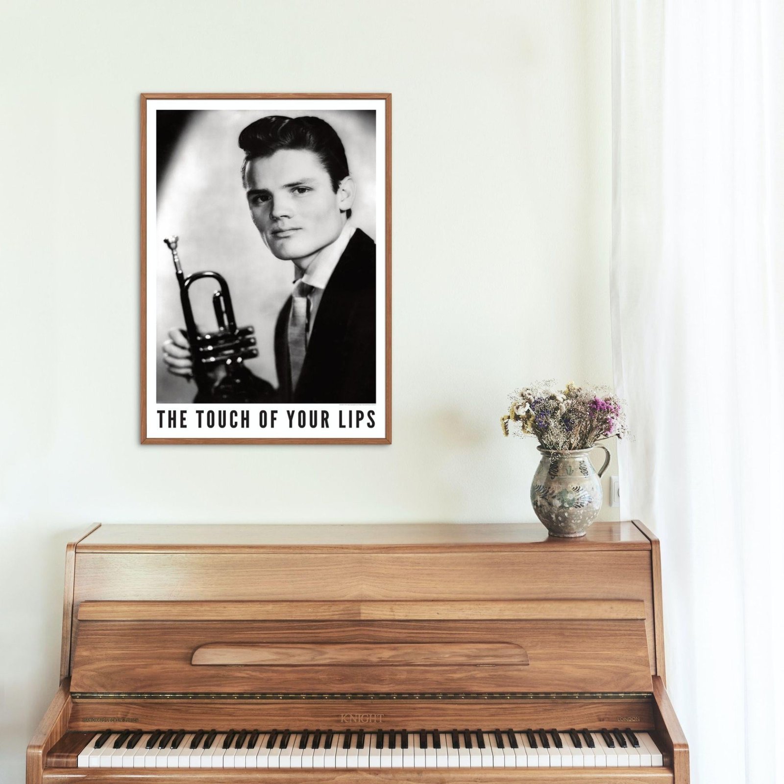 Framed poster above wooden piano with flower vase.