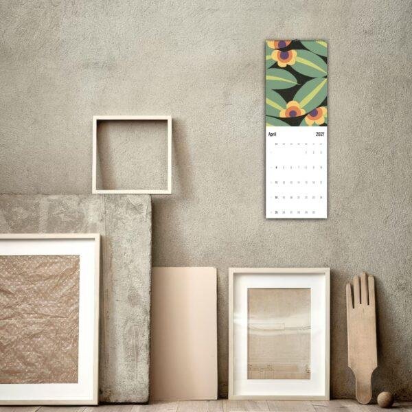April 2027 floral wall calendar hung above eclectic frames