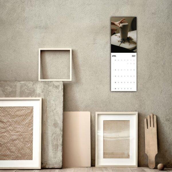 April 2027 wall calendar hanging above artistic frames