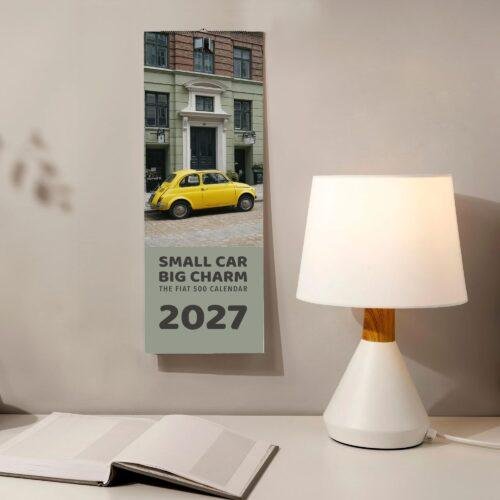 2027 Fiat 500 wall calendar hanging beside a desk lamp